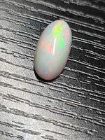 Oval Ethiopian opal cabochon on dark textured surface showing play of colour