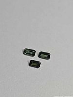 Three emerald-cut green sapphires on neutral background