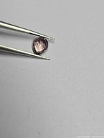 Pear cut purple-pink sapphire held by tweezers, table view