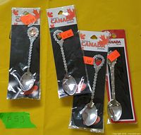 Four packaged Canada souvenir spoons on yellow surface
