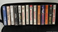 Front view of eighteen cassette spines inside black TDK case showing artist names
