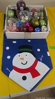 Box of assorted Christmas baubles and ornaments on snowman table runner