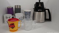 Group shot of carafe, tumblers, mugs including Flintstones glass and yellow plastic mug