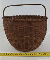 Front view of round woven wood basket showing handle and measuring tape for diameter