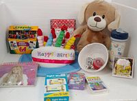 Overall lot showing crayons, plush dog, birthday hat, notebooks, water bottle, basket with dice, flash cards, photo album, card games