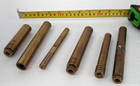 Six brass cylindrical laser casings lined beside measuring tape for scale