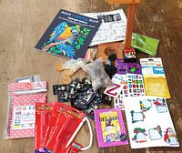 Full lot overview on tabletop showing coloring book, wrapping paper, sticker sheets, postage stamp booklets, pins, coins, patch and other small items