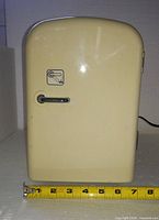 Front view of cream mini fridge with measuring tape showing width ~7 in