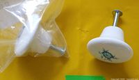 Two ceramic knobs, one in plastic bag showing screw hardware, one upright displaying blue flower design
