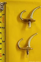 Two gold-tone double utility hooks beside measurement tape
