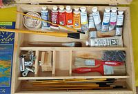 Contents of open wooden artist box: paint tubes, brushes, clips, mixing cups