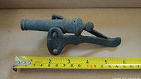 Side view of rusted cast iron toy cannon with tape measure showing length just under 6 inches