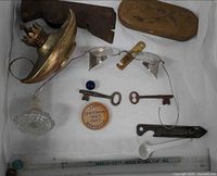 Overview of lot showing lamp part, glasses, keys, pin, marble, glass knob, spoon, opener bar and hatchet head