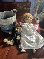 Group shot showing doll, teddy bear, woven basket, and knit blanket on table