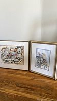 Both framed watercolor paintings standing against wall