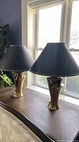 Pair of brass-tone table lamps with black shades on surface