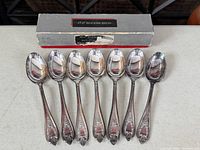 full view of seven teaspoons lined in front of original box
