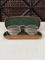 Open hard case displaying gold-tone eyeglasses with clear lenses