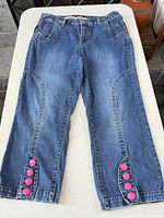 Full view of front side of capri jeans showing overall design and decorative buttons