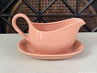 side profile of pink ceramic gravy boat on underplate