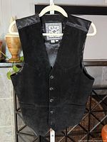 Front view of black suede leather vest on hanger showing five-button closure and brand label