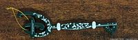 full view of green plastic key ornament with white floral pattern and gold hanging cord