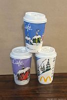 Three McCafé holiday paper cups stacked to show different prints and lids