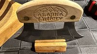 Close view of ulu knife on wood stand, showing handle branding and blade shape