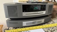 Front view showing Bose Wave Music System, display lit, CD slot, plus multi-CD changer base and remotes on top