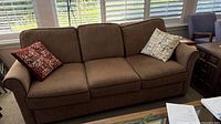 Full frontal view of brown three-seat sofa with both throw pillows visible