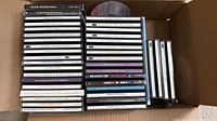 Open carton showing three columns of stacked jewel case CDs, assorted titles visible
