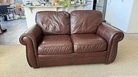 Front view of brown leather loveseat showing overall form, cushions and arms