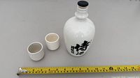 Bottle and two cups with measuring tape for scale