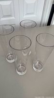 Four clear acrylic pilsner glasses standing upright