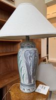 Full view of one lamp standing on table showing elephant design and shade