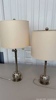 Two chrome table lamps with ivory shades on surface