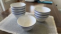 Eight stacked white bowls with blue stripes on placemat