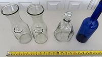 Group shot of two clear carafes, clear decanter with stopper, blue bottle with measuring tape