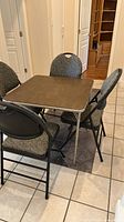 Square folding card table with four folding chairs arranged around it