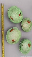 Seven green lettuce leaf plates with red tomato accents, tape measure for scale