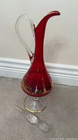 Full view of ruby glass decanter showing shape, clear handle, broken stopper pieces