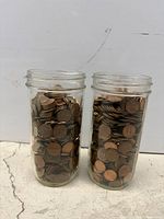 Front view of two tall glass jars packed with US pennies
