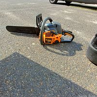 Poulan orange and black chainsaw with 18-inch bar lying on asphalt, partial view of black case