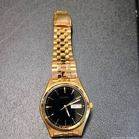 Front view of gold Seiko wristwatch showing black dial and day-date