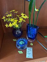Three art glass pieces: round vase with yellow flowers, scalloped dish with stones, tall vase with glass flower