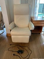 Front view of beige leather Stressless recliner with power cord on floor