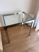 Overall view of rectangular side table showing clear glass top and chrome legs on wood floor