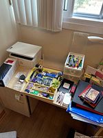 Printer, sealed toner box, desk lamp, drawer organizer, tray of assorted office supplies, stack of notebooks and folders on desk