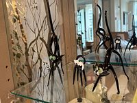 Two black hand-blown glass cat figurines and small white cat on ring stand displayed on glass shelf