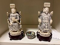 Front view of two carved figures on stands with porcelain bowl between